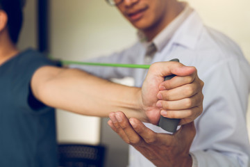 Asian male physical therapist descent working and helping to protect the hands of patients with patient doing stretching exercise with a flexible exercise band in clinic room.