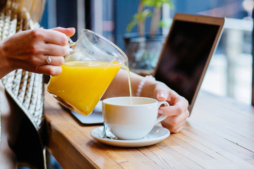 Positive thoughtful female distance worker in cafe drinking sea buckthorn tea. Rest in the weekend in your favorite cafe, mature businerss woman traveler sits in cafe over cup of yellow tea pouring it