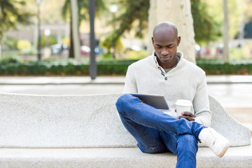 Black young man with tablet computer and take away coffee