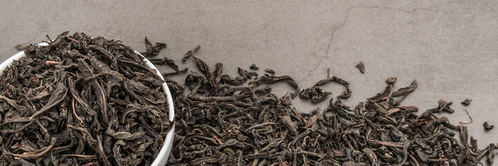 Dried tea is poured into a white ceramic cup on a gray textured background.