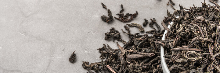 Dried tea is poured into a white ceramic cup on a gray textured background.