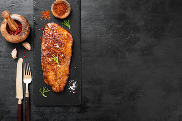 Grilled beef steak with rosemary, salt and pepper on black stone plate. Top view