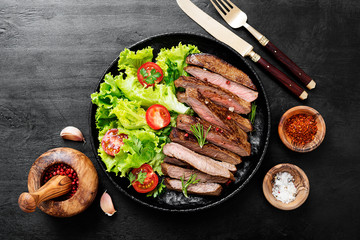 Sliced grilled beef steak and green salad leaves on black plate.Top wiev.