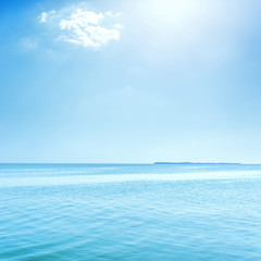 blue sea with island on horizon and clouds in sky with sun