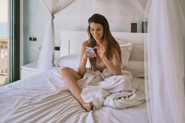 a young woman in underwear on her bed using a mobile phone