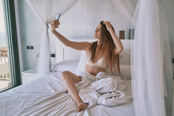 a young woman in underwear on her bed taking a selfie