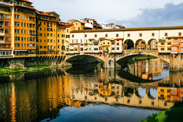 Fototapeta na wymiar Old bridge Ponte Vecchio with colourful buildings houses and its reflection in the river Arno in Florance, Tuscany, Italy. April 2012
