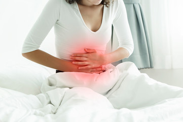 Young woman suffering from abdominal pain while sitting on bed.