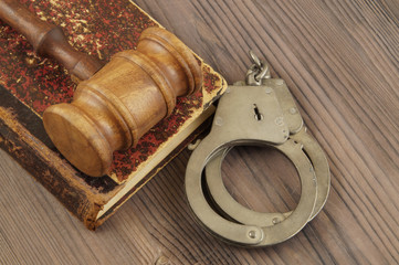 Wooden gavel, handcuffs and old legal book on table