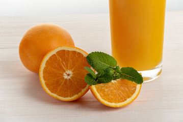 A glass of fresh orange juice on a white wooden surface with slices of orange and mint.