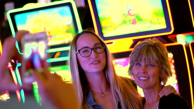 This video shows a man taking a cell phone photo of a smiling mother and daughter in a lively casino.