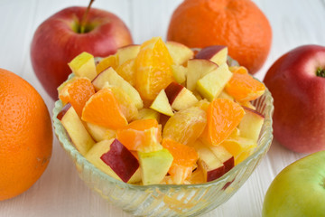 Bowl of healthy fresh fruit salad on wooden background. Citrus fruits on a white background. Oranges, tangerines, apples.