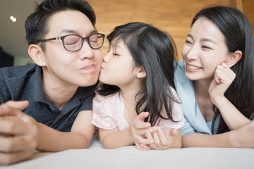little daughter kissing Parents on cheeks. Asian family portrait.