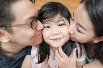 Asian Parents kissing their little daughter on both cheeks. family portrait.