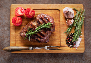 top view of grilled rib-eye steak with herbs and vegetables on wooden board