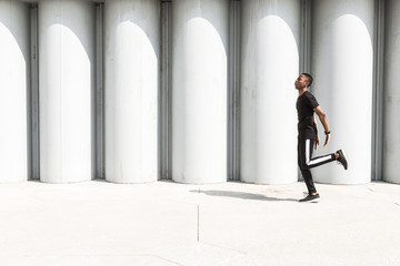 Athletic young afroamerican man running on the promenade. Black Male runner sprinting outdoors. Healthy lifestyle concept.