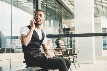 Young african american business man in suit and eyeglasses talking on the phone on the background of the business center