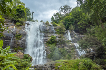 The grand waterfall in the nature park with the greenery trees and forest in the nice day.