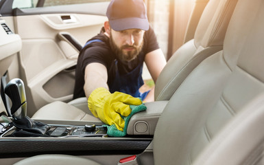 Cleaning service. Man in uniform and yellow gloves washes a car interior in a car wash. Worker...