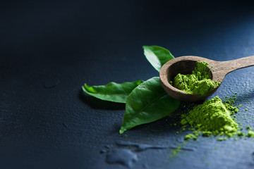 Matcha tea powder in wooden spoon with tea leaves on a dark background with copy space