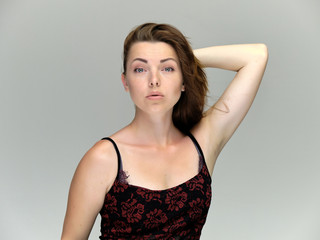 Fototapeta premium Closeup portrait of pretty girl, brunette woman 30 years old on a light gray background with beautiful dark hair and excellent skin of the face and body. She shows emotions, smiles, wonders.