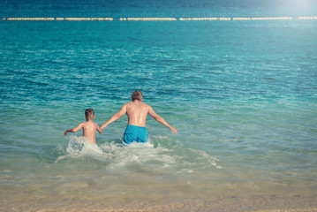 European man is happy to spend his summer holidays with his son. They are swimming in the ocean and enjoying pastime.