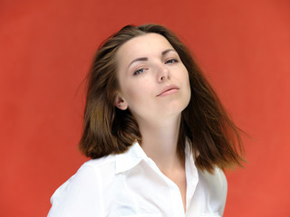 A close-up portrait of a pretty girl, a brunette woman of 30 years old on a red background in a white shirt with flowing dark hair and excellent skin. She shows emotions, smiles, wonders.