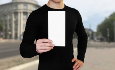 A man holding a white sheet of paper. Holding a booklet. Close up. The background of the city