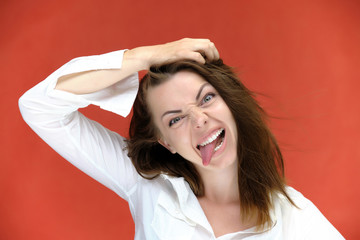Naklejka premium A close-up portrait of a pretty girl, a brunette woman of 30 years old on a red background in a white shirt with flowing dark hair and excellent skin. She shows emotions, smiles, wonders.