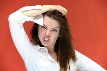 A close-up portrait of a pretty girl, a brunette woman of 30 years old on a red background in a white shirt with flowing dark hair and excellent skin. She shows emotions, smiles, wonders.