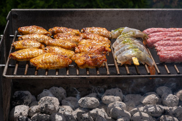 Mixed assortment of marinated meat, chicken, and prawns grilling on hot coals on a BBQ