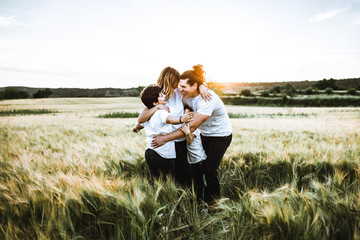 Naklejka na ściany i meble Happy family hugging in the field and smiling. Family in a sunset