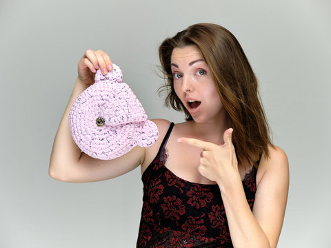 Closeup portrait of pretty girl, brunette woman 30 years old on a light gray background with a gift in a small handbag with dark hair and excellent skin of face. She shows emotions, smiles, wonders.