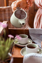 A woman pours tea into a mug of tea. Cozy atmosphere and homemade breakfast at home. Toned photo.