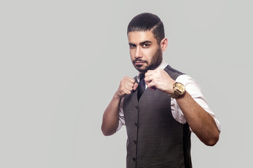 Portrait of serious bearded man in white shirt and waistcoat standing with boxing fists and looking at camera with aggressive face and ready to attack. indoor studio shot isolated on gray background.