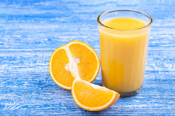 A glass of orange juice near which lay sliced oranges. View from above.