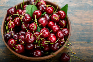 Fresh sweet cherries bowl with leaves  on a wooden table