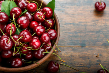 Fresh sweet cherries bowl with leaves  on a wooden table