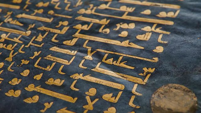 The Blue Qur'an manuscript in Kufic calligraphy written in gold and silver on indigo-dyed parchment, shallow depth of field close-up slow tilt up CGI shot.