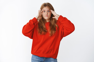 Girl shocked cannot understant what happening standing confused and perplexed with mind blowing out from information holding hands on temples lifting eyebrows questioned wearing red sweater