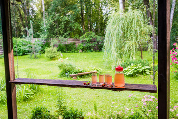 Long wooden table with four full glasses and jug of fruit juice on terrace. Summertime in...