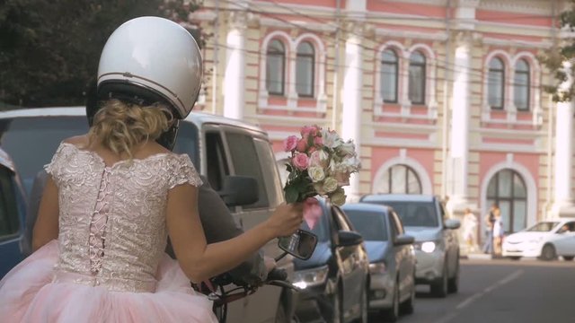 Newlywed couple drive around the city by motorcycle through traffic in summer city. Life style idea concept. Bride is holding wedding bouquet. Young beautiful couple rides through the city streets, fr