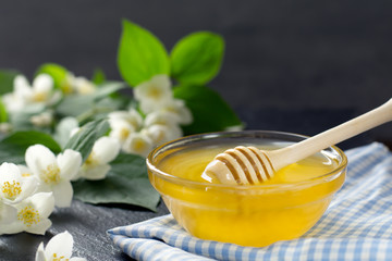 fragrant golden honey in a glass jar with a wooden spoon is located near a branch with jasmine flowers