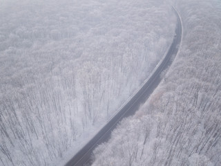 Aerial view of asphalt road through the snowy forest with single car, natural winter background