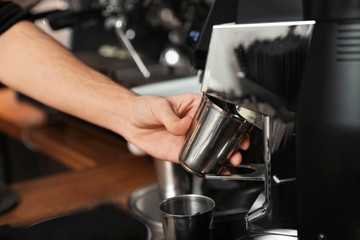 Fototapeta na wymiar Barista with metal cup using coffee grinding machine in cafe, closeup
