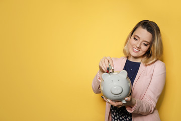 Beautiful businesswoman putting money into piggy bank on color background. Space for text