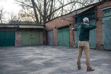 Fototapeta premium young guy in a white baseball cap shoots a bow. archer is training on the street. a man stands with his back to the camera and shoots a bow.