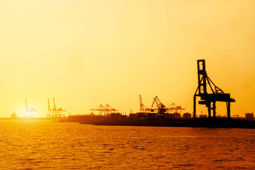Obraz premium Silhouette of container and gantry crane at Osaka port are loading on evening with sunset glow background.