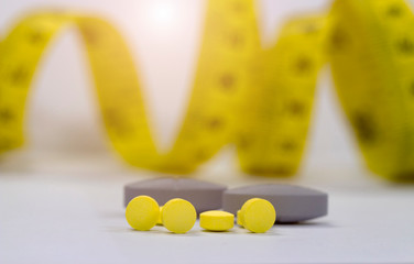Diet concept; Slim with pills, dangerous for health.Yellow pills with blurred yellow measuring tape...