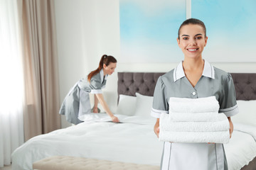 Chambermaid with stack of fresh towels in hotel room. Space for text